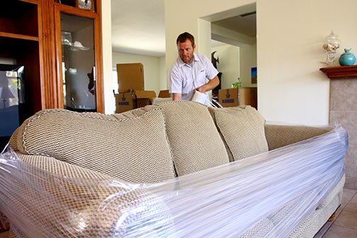 Man with and tan couch in a home getting wrapped for moving..