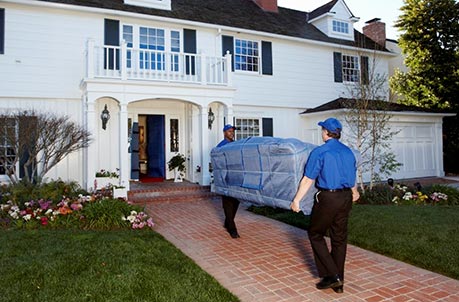 Two men moving a blue covered couch into a white and black home. 